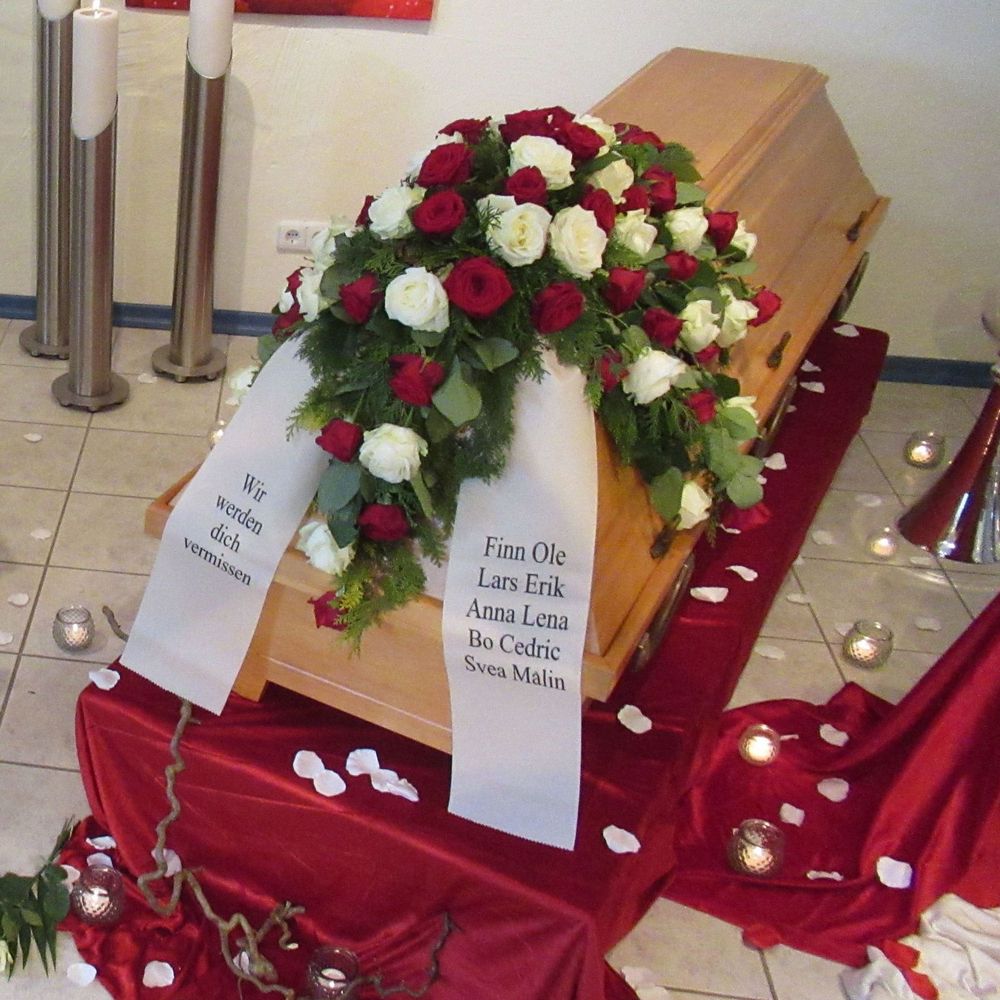 Trauergesteck mit weißen und roten Rosen auf einem Sarg